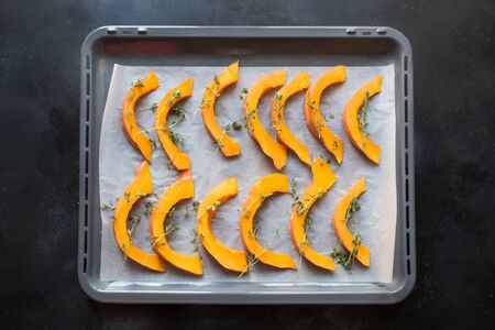 Hot roasted sliced pumpkin with thyme, olive oil and salt on dripping pan. Tasty vegan snack. Food pattern.の写真素材