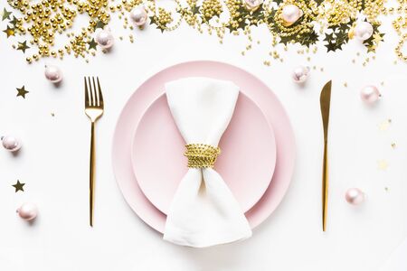 Christmas table setting with pink dishware, golden silverware and party decorations on white background. Top view. Xmas dinner.の写真素材