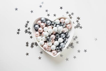 Christmas white, pink, grey silver balls in plate shape of heart decorated confetti stars on pink background. Top view. Xmas concept. Love holiday New Year.の写真素材