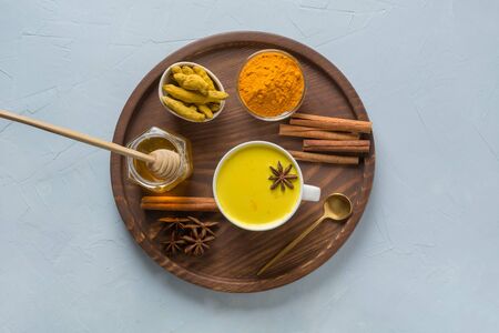 Golden turmeric milk with curcuma powder, honey and spices on light blue background. Healthy drink...