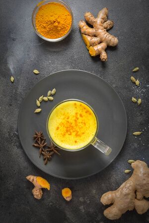Cup of ayurvedic golden turmeric latte milk with curcuma powder and anise star on black. Top view. Healthy drink for improve immunity. Flat lay composition.の写真素材