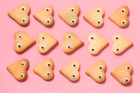 Homemade heart shaped cookies decorated cartoon eyes as face on pink background. Top view. Copy space. Valentines day greeting card. Flat lay. Food pattern.の写真素材