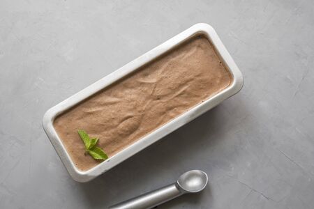 Banana chocolate homemade ice cream in metallic container on grey concrete background. Space for...
