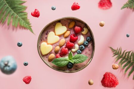 Healthy smoothie for breakfast decorated banana, blueberry, nuts in coconut bowl on pink background. View from above. Clean eating. Food levitation.の写真素材