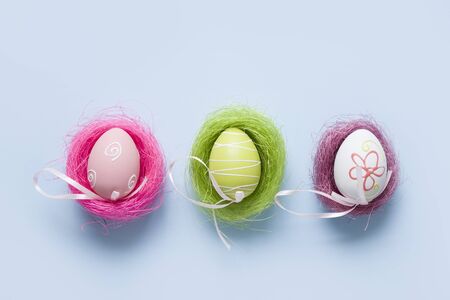 Colorful pastel eggs in three nests. Easter minimal creative composition on blue. Greeting card.