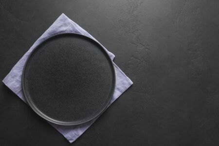 Empty black plate with lilac towel on black kitchen background. View from above. Space for your design, recipe or menu.の写真素材