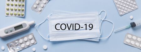Different types protective medical face mask, pills, thermometer on blue. View from above. Prevention of virus. Text: COVID-19. Banner.の写真素材