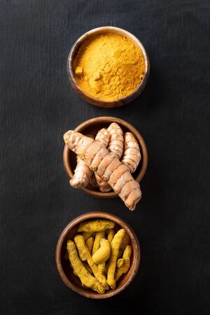 Fresh and dry root turmeric, curcuma powder in bowl on black table. Healthy spice immunity. Top view. Natural antiseptic.の写真素材