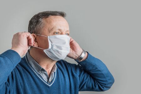Adult man puts on medical surgical mask to protect against virus Covid 19. Space for text. Prevention of Coronavirus.の写真素材