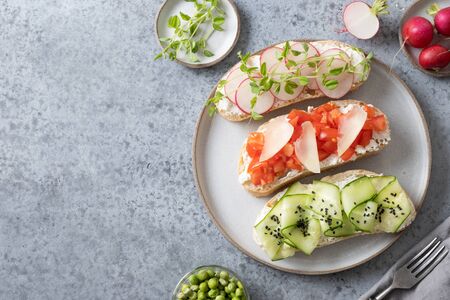 Three sandwiches with fresh vegetables, radishes, tomatoes, cucumbers and microgreens on grey background. View from above. Copy space.の写真素材