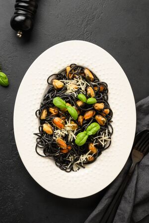 Black pasta spaghetti squid Ink with mussels in white plate on black background. Top view. Copy space.の写真素材