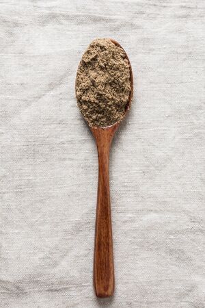 Flax flour in wooden spoon on linen tablecloth. Top view. Vertical format. Close up.の写真素材