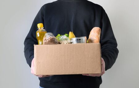 Volunteer holding donation food with goods. Box with oil, vegetables, canned food, cereals, fruits. Delivery food.の写真素材