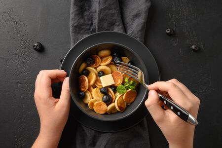 Child tries homemade tiny pancake with blueberries on black background. View from above. Close up. Trendy tasty breakfast.の写真素材