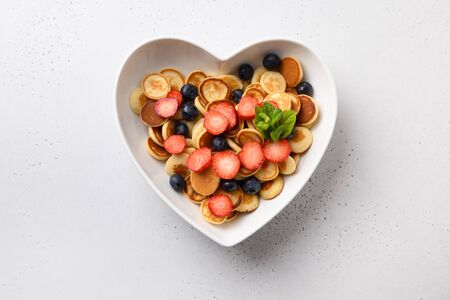 Trendy tiny pancakes with blueberry and strawberry in plate shaped of heart on white background. View from above.の写真素材