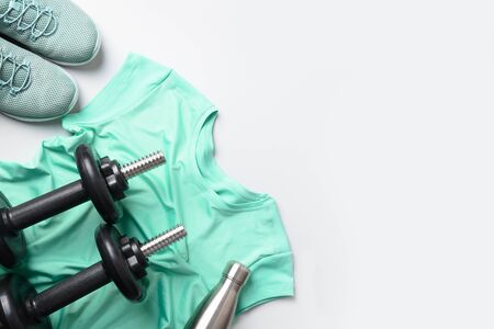Sport and fitness equipment, female tee-shirt, black dumbbells, shoes, water bottle on grey. View from above, space for your text.の写真素材