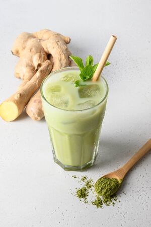 Iced Green matcha tea and pouring milk in latte glass with ginger on white table.Close up. Vertical orientation.の写真素材