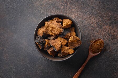 Chaga birch edible mushrooms in bowl on natural dark brown table. View from above. Close up.