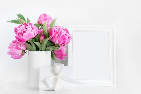 Pink peony in white vase, gift and photo frame. White interior. Space for text.の写真素材