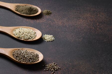 Organic dried hemp seeds, flour, kernels in three wooden spoons on brown background. Close up. Healthy ingredients for clean eating and vegan.の写真素材