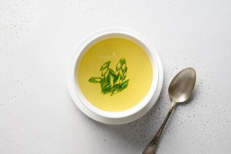 Chicken broth with onion, greens in white bowl isolated over white table. Copy space.の写真素材