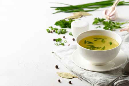 Chicken broth with spices, greens, garlec, parsley, onion in white bowl on white table. Copy space. Close up.の写真素材