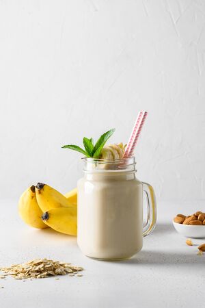 Banana milkshake with oatmeal and almond nuts in mason jar on white board. Vertical formatの写真素材