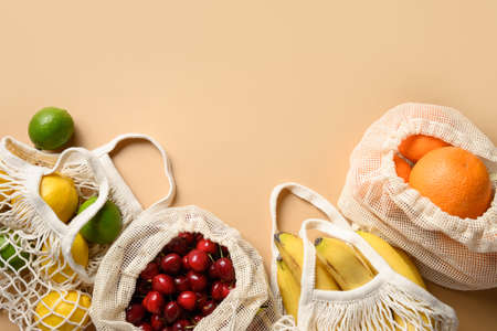Fruits, berries and citrics in mesh bags on beige background. Zero waste shopping. Ecological...