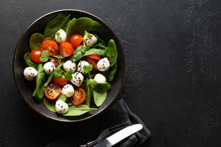 Summer salad with spinach, cherry tomatoes and Mozzarella cheese on black background. Copy space.