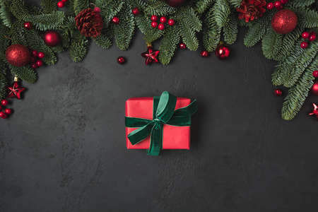 Christmas frame with red gift and decor, fir branches on black background. Xmas greeting card. Happy...