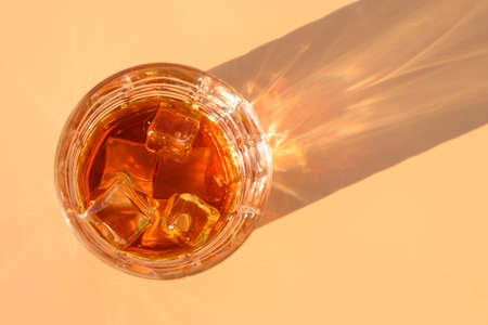 Glass of cold whiskey on beige background with sunny shadow. Copy space. View from aboveの写真素材
