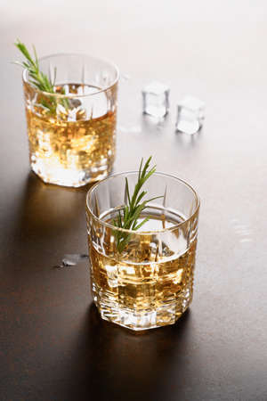 Two glasses of cold whiskey with rosemary sprig on dark background. Vertical orientation. Close up.の写真素材