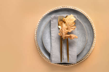 Fall table setting with golden cutlery decorated autumn oak leaf on beige background. View from above. Space for design.の写真素材