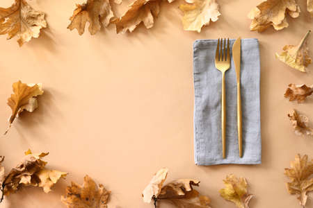 Fall oak leaves as frame and golden cutlery on beige background. View from above, space for design....