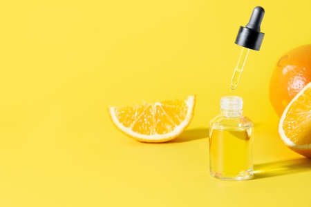 Cosmetic hyaluronic acid or hydrating oil and orange essence in glass bottle with flying pipette on...