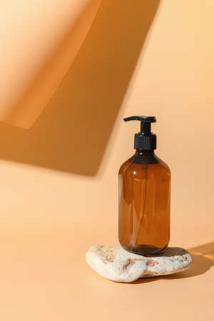 Glass bottle for soap, SPA, cosmetic care on stone podium. Monochrome vertical creative composition with shadow on beige background.の写真素材