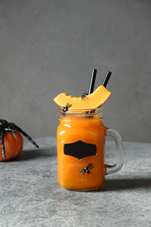 Halloween Cocktail with pumpkin juice, spice, carrot garnish spiders for festive party on gray....
