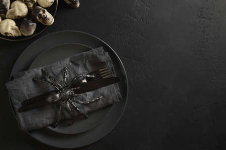 Halloween table setting with skulls and big spider on black dark table. View from above. Copy space.
