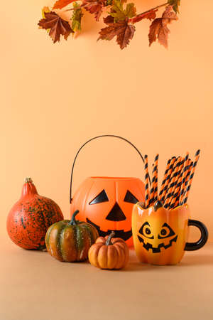 Halloween fun party decorations, candy bowl, pumpkins, sweets, mug with drinking starw r on orange background. Vertical composition with copy space.の写真素材