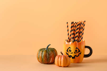 Halloween fun party decorations, pumpkins, mug with drinking straw on orange background. Horizontal composition with copy space.の写真素材