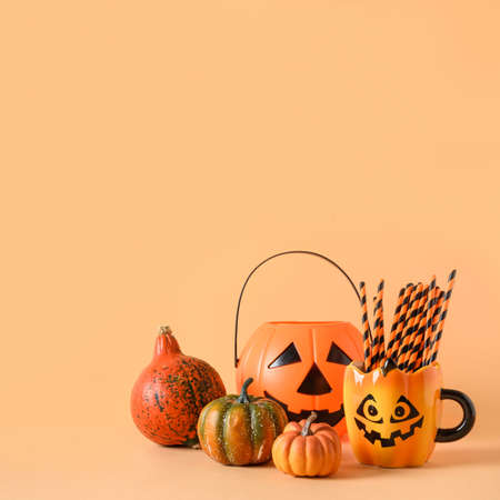 Halloween festive party decorations, candy bowl, pumpkins, funny mug with drinking straw on orange background. Square composition with copy space.の写真素材
