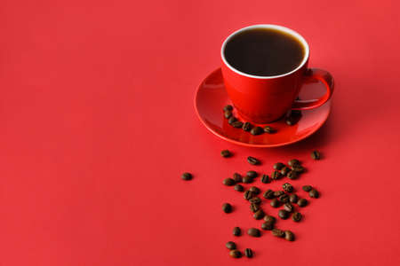 Red cup of coffee and beans on red background. Copy space. Close up.