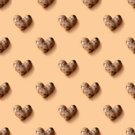 Seamless pattern of abnormal potato in shape of heart on beige background.