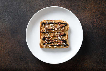Crispy sandwich with peanut paste in white plate isolated on brown background. Healthy breakfast. View from above.の写真素材