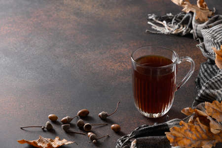 Autumn acorn coffee in cozy lifestyle on brown table with fall oak leaves and cozy scarf. Coffee...