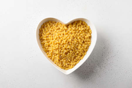 Raw ditalini pasta in white plate in shape of heart on white background. View from above.の写真素材