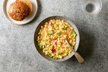Fresh homemade soup of peas, greens, tomatoes, ham, ditalini soup pasta egg on gray table. View from above.の写真素材