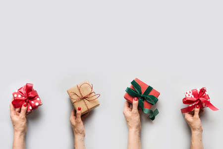 Female hands holding different Christmas gifts on gray background. Greeting card with copy space....