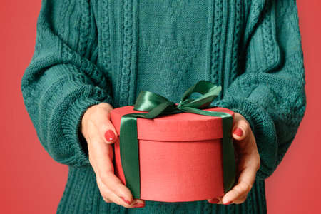 Christmas holiday red gift with red bow in woman hands in green sweater. Xmas holiday banner.の写真素材