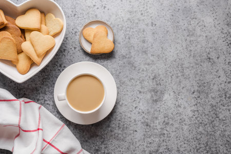 Cup of milk coffee and handmade cookies in shape of heart on grey stone background. Valentines Day card. Flat lay, top view, copy space.の写真素材